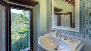 Une salle de bain avec un grand lavabo, un miroir et une fenêtre donnant sur un paysage verdoyant.