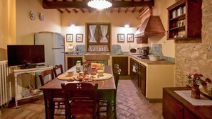 A cozy kitchen with a dining table, chairs, a television, and a refrigerator.