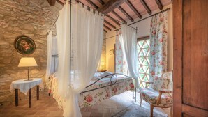 A bedroom with a four-poster bed, floral curtains, a round table with a lamp, and a chair. - Amazing apartment in Casole d'Elsa with WiFi (Casole d'Elsa)