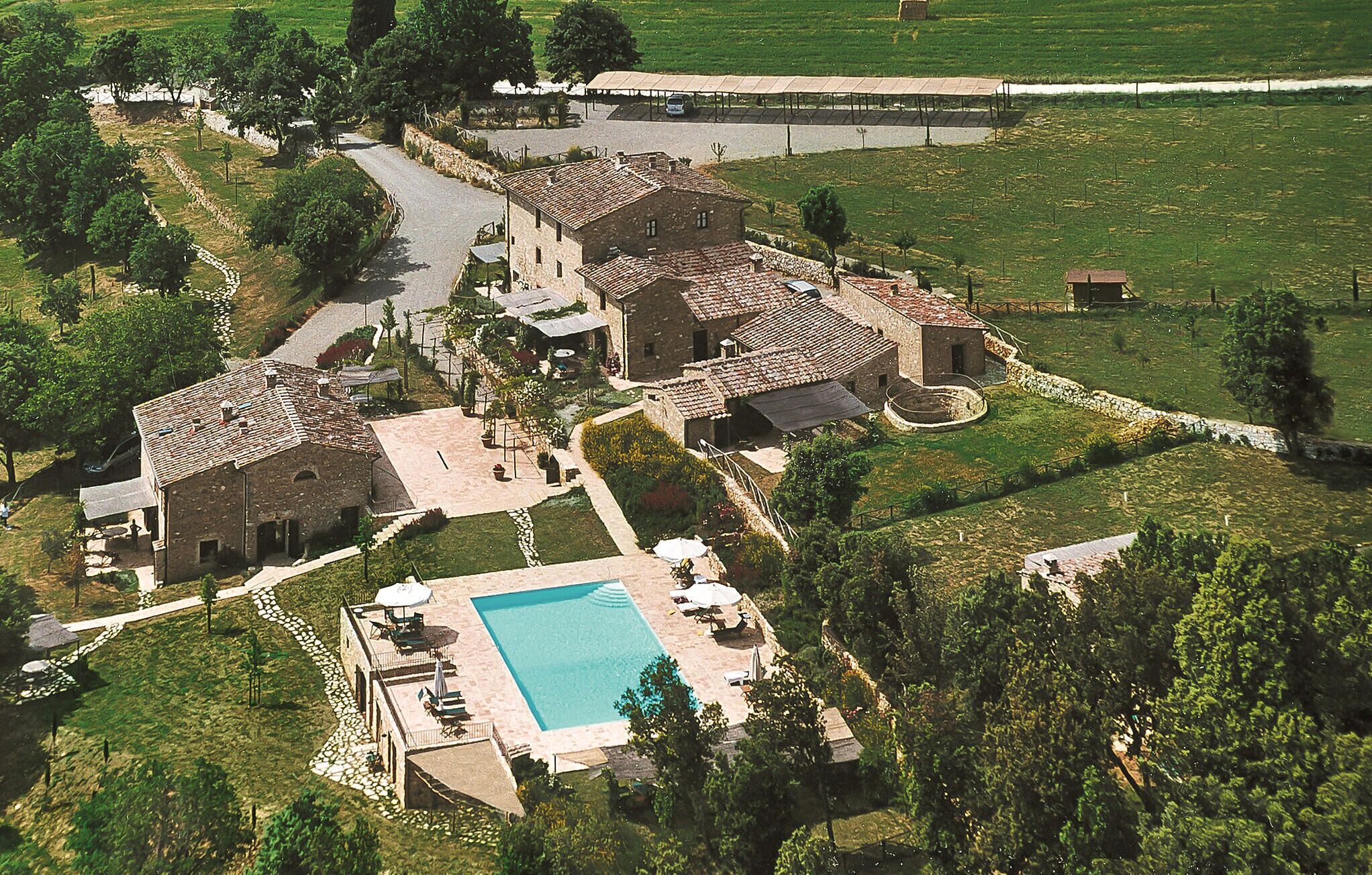 A large villa with multiple buildings, a swimming pool, and surrounding green fields.