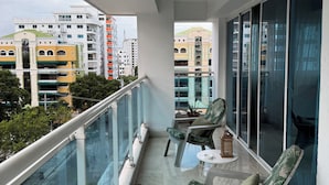 A balcony with a glass railing, two chairs, a small table, and a lantern.
