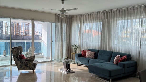 A spacious living room with a large sectional sofa, a glass coffee table, and a patterned armchair.