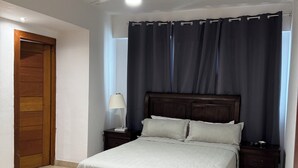 A bedroom with a bed, a nightstand, a lamp, a ceiling fan, and a door.