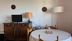 Ein Essbereich mit einem runden Tisch, bedeckt mit einer karierten Tischdecke, einem Holzschrank mit Fernseher, einer Lampe und einem Radio.