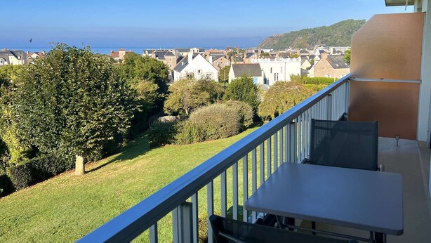 Ein Balkon mit Tisch und Stühlen, der auf einen Wohnbereich mit Häusern und Meerblick blickt.