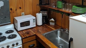A kitchen with wooden walls, a stove, a microwave, a sink, and shelves with dishes and glasses.