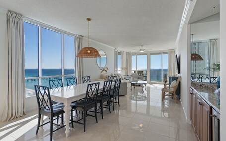 A spacious living area with a large dining table, multiple chairs, a sofa, and a view of the ocean.