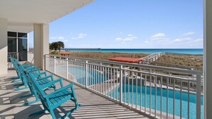 Un balcon avec une piscine, des chaises et une vue sur la plage et l’océan.