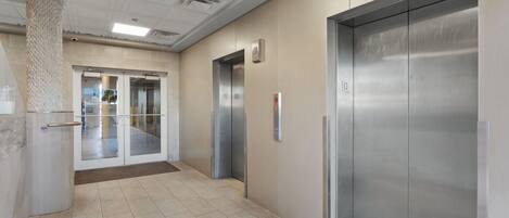 Un área de ascensor moderna con acceso por puerta de vidrio y puerta de ascensor metálica.