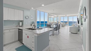 A modern kitchen with white cabinets, a central island, and a view of the ocean. - Luxurious Gulf-front Condo, Heated Pool, Spa/Gym (Navarre Beach)