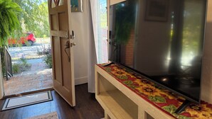 A room with a large flat-screen TV on a wooden stand, a door leading outside, and a small table with a floral table runner. - Charming 1-bedroom house in Culver City (Culver City)