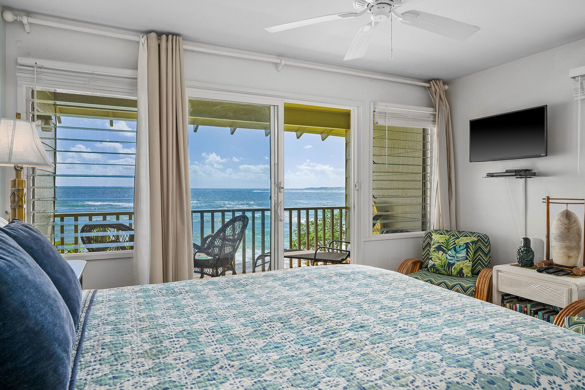 A bedroom with a bed, a TV, and a balcony with a view of the ocean.