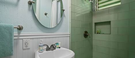 A bathroom with a white sink, a round mirror, and a shower area with green tiles.