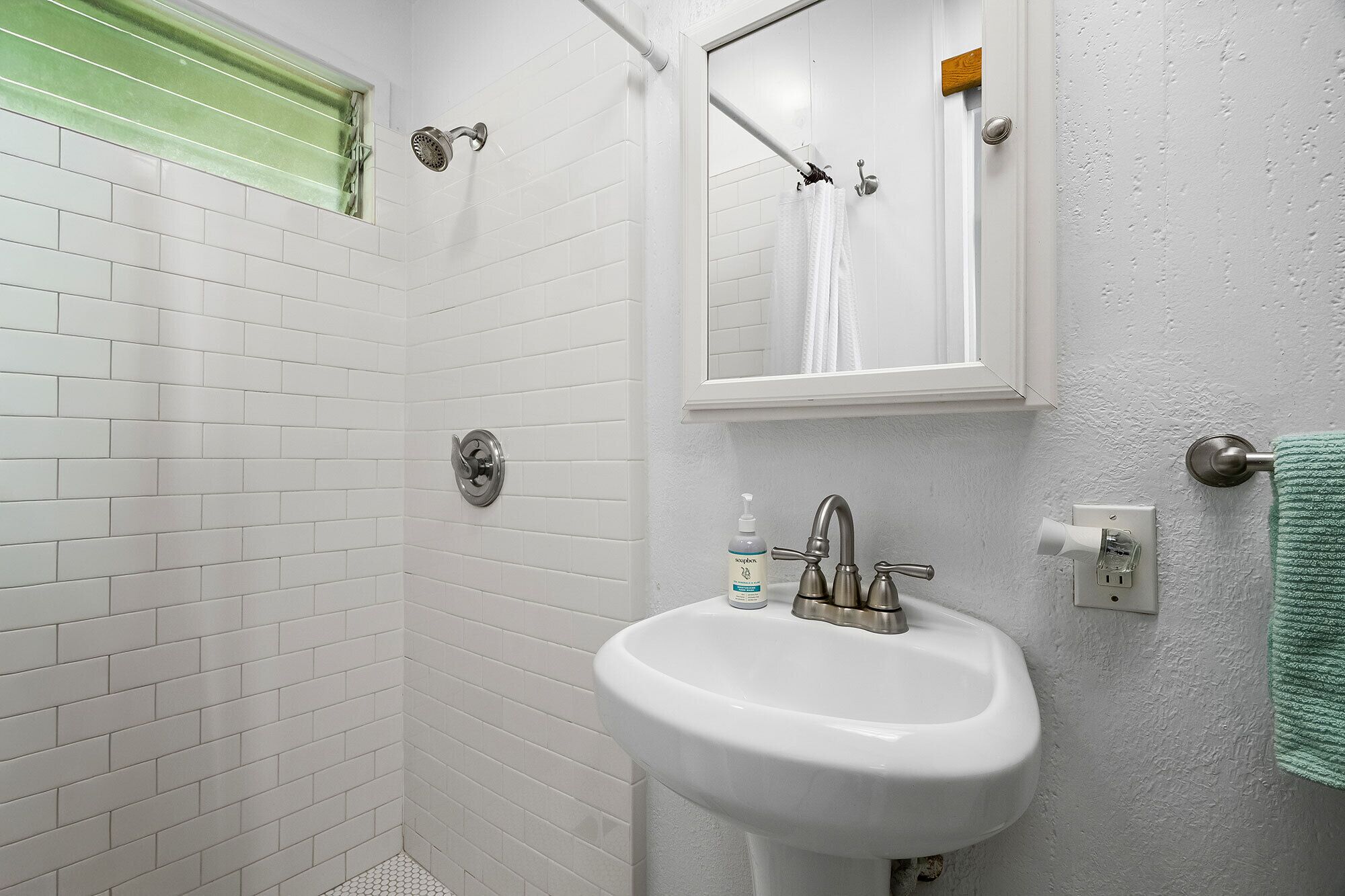 A bathroom with white subway tiles, a white sink, a shower with a handheld showerhead, a mirror, and a towel rack.