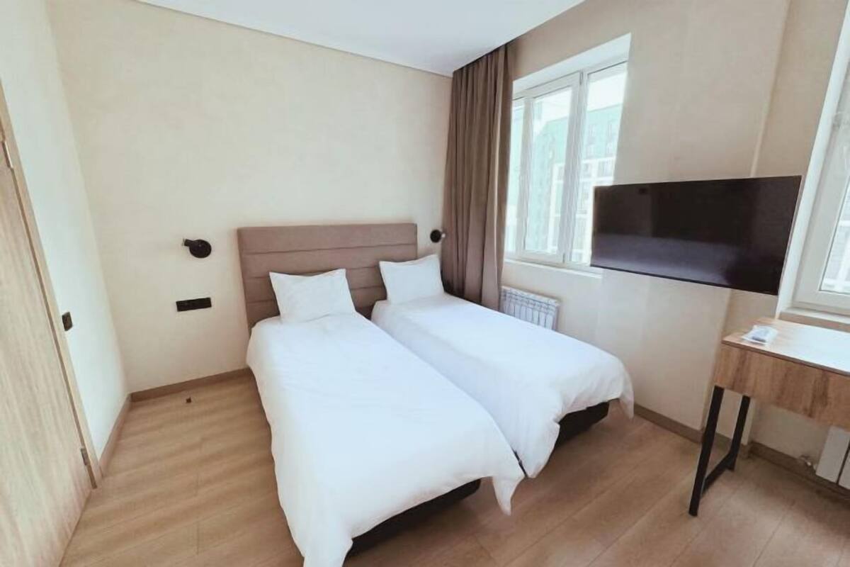 Une chambre d’hôtel avec deux lits simples, une télévision, un bureau et une fenêtre avec des rideaux.