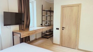 A bedroom with a wooden desk, a television, a wardrobe, and a shelf unit. - Tan Hotel Astana (Astana)