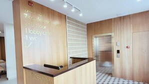A hotel reception area with a wooden reception desk, a wall-mounted directory, and a patterned floor. - Tan Hotel Astana (Astana)
