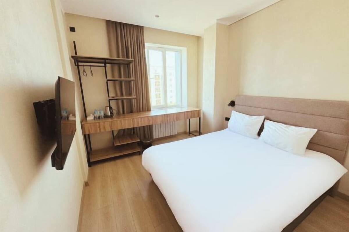 Une chambre d’hôtel avec un lit, un bureau et une chaise, une télévision et une fenêtre avec des rideaux.
