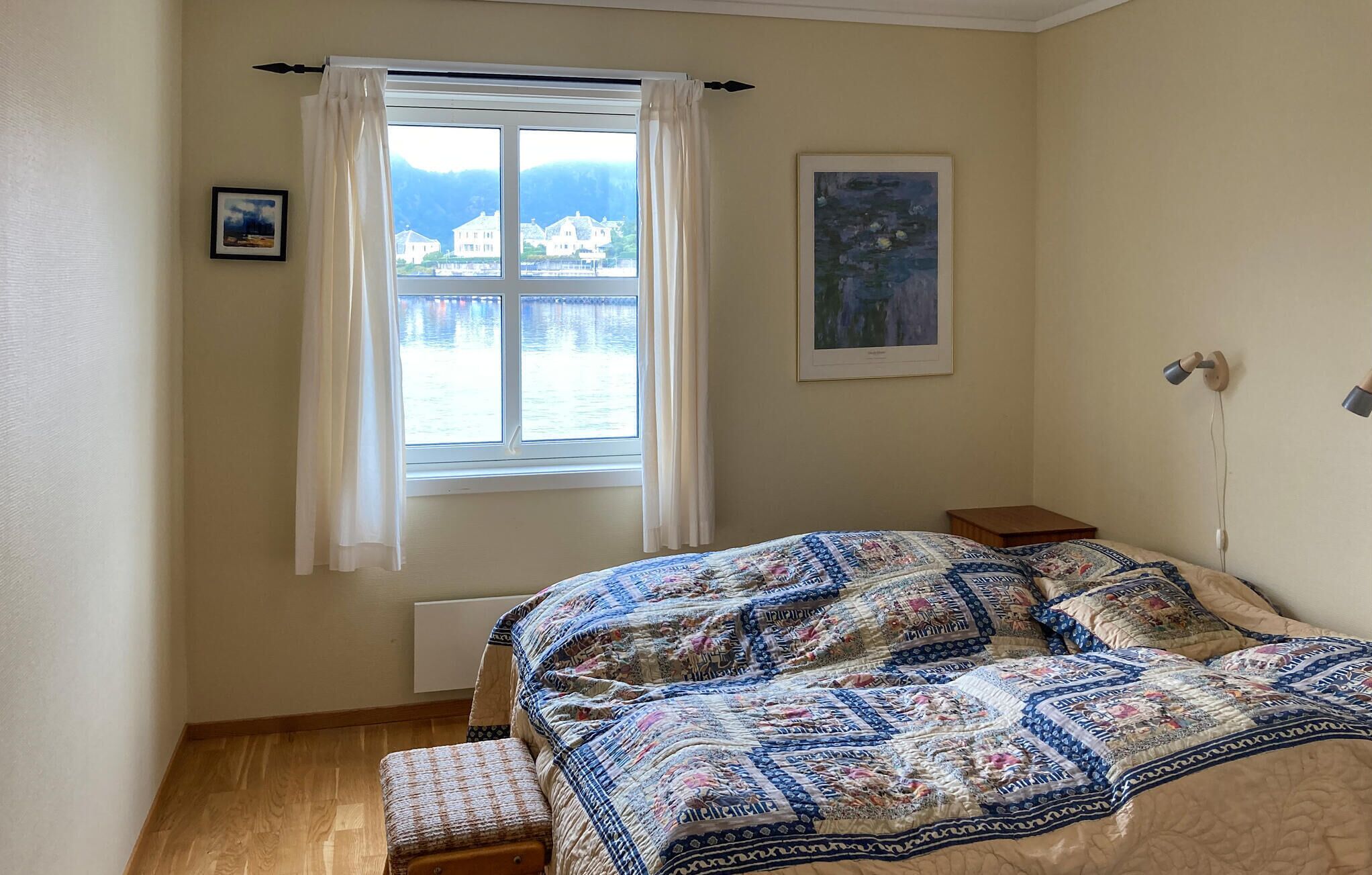 Una camera da letto con un letto grande, una finestra con tende, un quadro appeso al muro e un comodino.