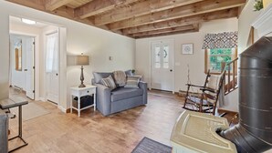 A spacious living room with a wooden ceiling, a grey sofa, a rocking chair, and a large fireplace.