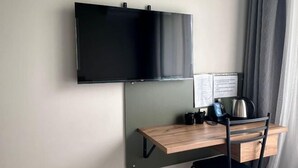 A room with a mounted TV, a desk with a chair, a kettle, and a cup. - Gul Dala apartments (Almaty)