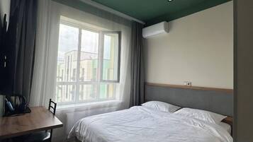 A hotel room with a bed, a table, and a window with curtains.