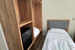 A single bed with a wooden headboard, a small black refrigerator, and a wooden wardrobe.