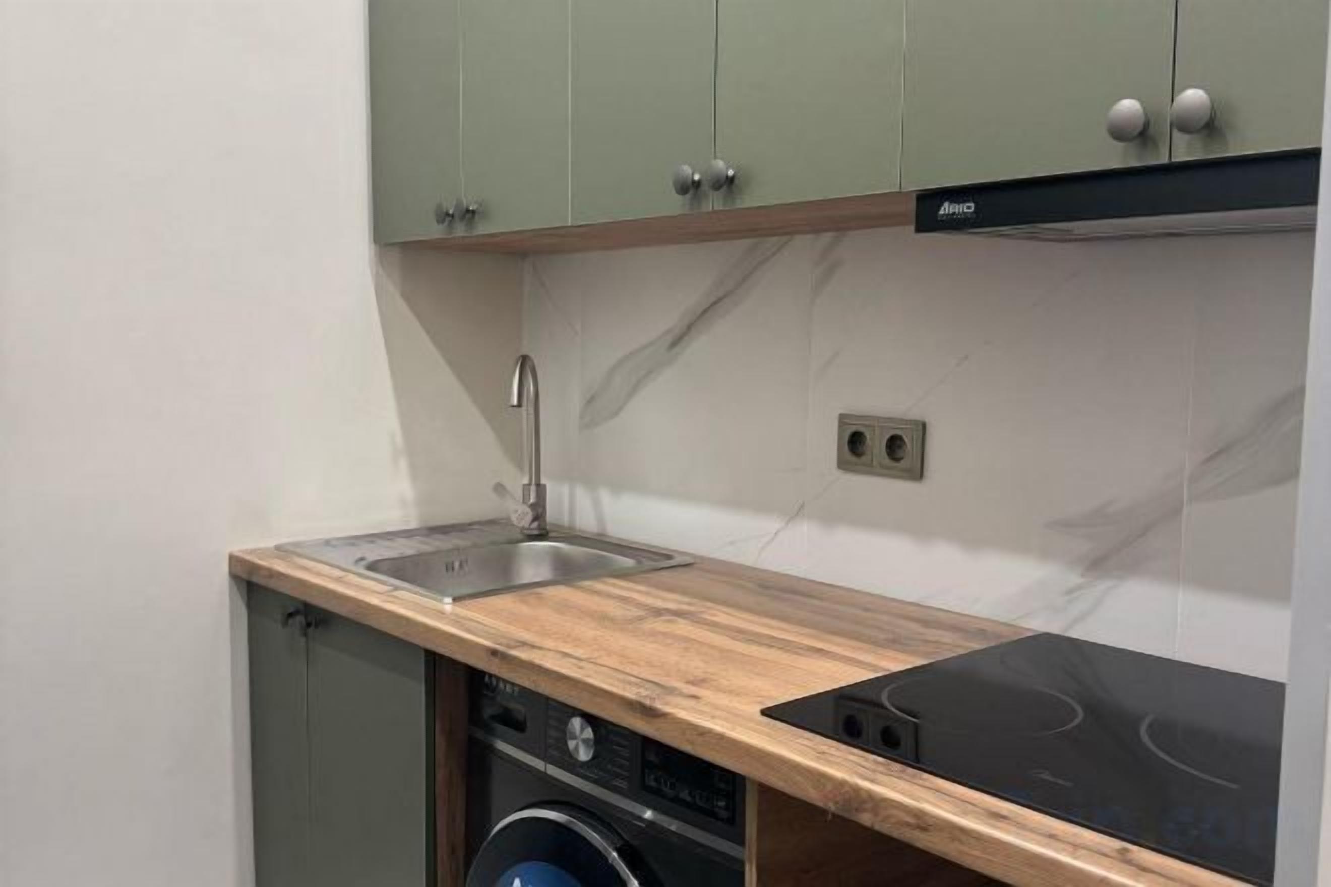 A compact kitchen with a built-in dishwasher, a sink, and a black induction cooktop.