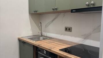 A compact kitchen with a built-in dishwasher, a sink, and a black induction cooktop.