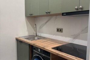 A compact kitchen with a built-in dishwasher, a sink, and a black induction cooktop. - Gul Dala apartments (Almaty)
