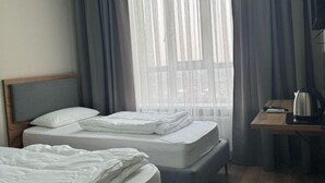A hotel room with two beds, a wooden desk, a kettle, and sheer curtains. - Gul Dala apartments (Almaty)