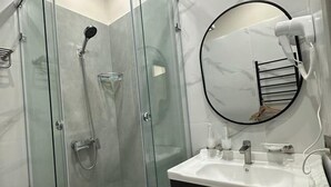 A modern bathroom with a glass-enclosed shower, a round mirror, and a white sink with a black countertop. - Gul Dala apartments (Almaty)