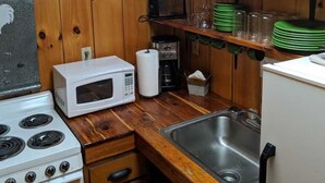 A kitchen with wooden walls, a stove, a microwave, a sink, and shelves with dishes and glasses. - Immerse yourself in nature at High Ridge Cabin 3 (Mauckport)