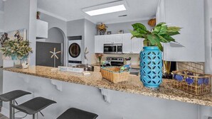 A modern kitchen with white cabinets, a granite countertop, a large blue vase, and a sign that says "Seas the Day".
