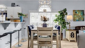 A modern kitchen with a dining table, bar stools, and a chandelier.