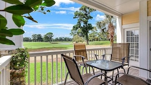 A covered patio with a table and chairs, overlooking a golf course.