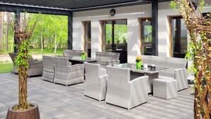 Un patio exterior con mobiliario de mimbre, una mesa de vidrio y vistas a un bosque.