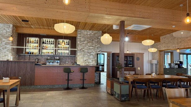 Un restaurante con zona de bar, techo de madera, paredes de piedra y área de comedor con mesas y sillas.