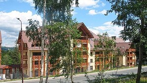 Une rangée d’immeubles à plusieurs étages, dotés de balcons, avec une route pavée devant et des arbres au premier plan.