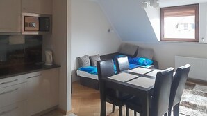 Une pièce compacte comprenant un coin cuisine, un lit avec une literie bleue et un espace repas avec une table et des chaises.