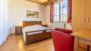 A bedroom with a wooden bed, a red chair, a wooden table, a painting on the wall, and a window with curtains. - La Vigneraie - FUISSE (FUISSE)