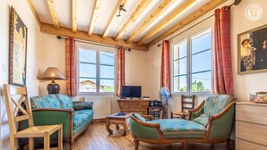 A cozy living room with wooden beams, a sofa, a chair, a TV, and a table. - La Vigneraie - FUISSE (FUISSE)