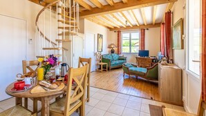 A cozy room with a spiral staircase, wooden furniture, a dining table with breakfast items, and a view of greenery outside. - La Vigneraie - FUISSE (FUISSE)