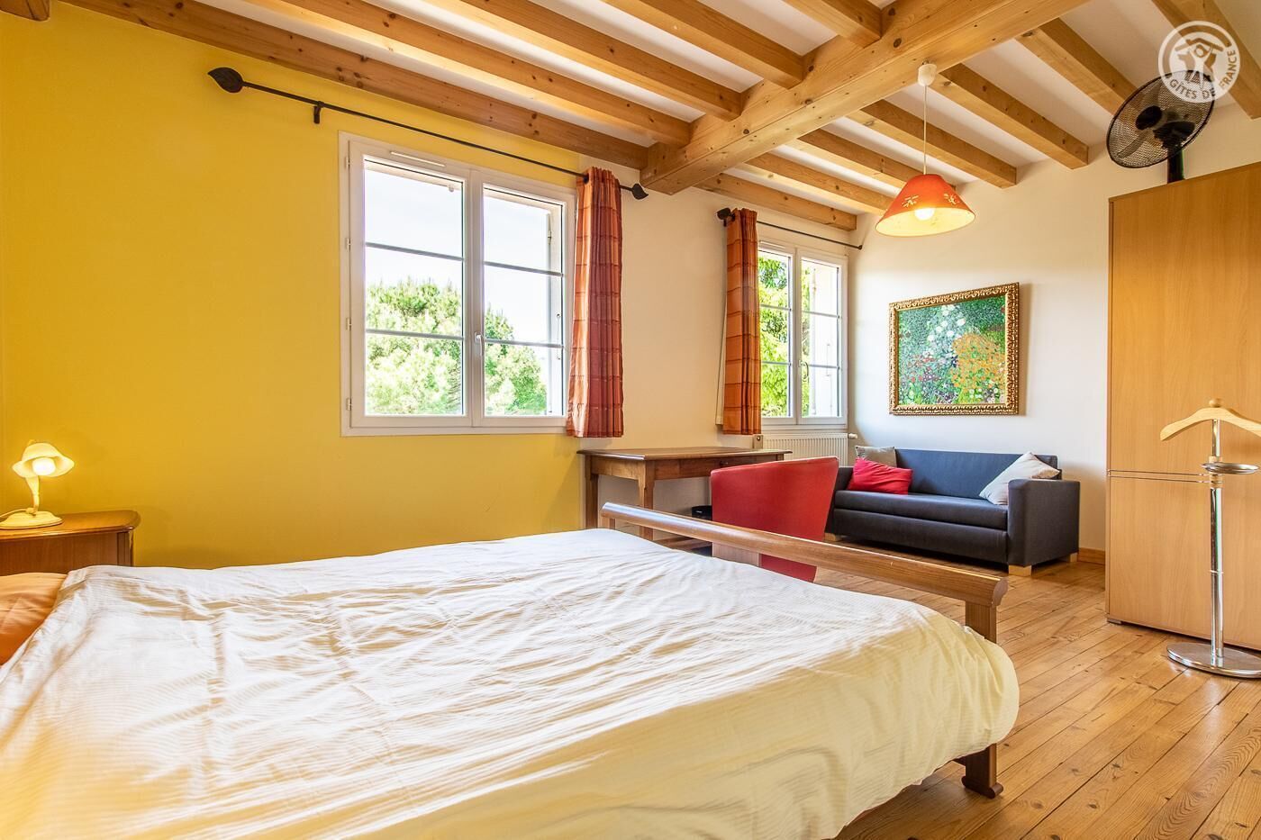 Ein Schlafzimmer mit einem großen Bett, einem Schreibtisch, einem roten Sessel, einer Couch und einem Kleiderschrank.