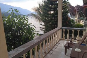 A balcony with a view of a body of water and mountains, accompanied by a table and chairs. - Sibayak Guest house (Samosir Regency)