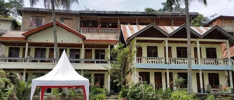 A multi-story building with balconies, a covered outdoor seating area, and a stone pathway leading to the entrance.