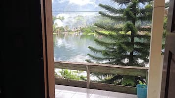 A view from a room with a wooden railing overlooking a body of water, surrounded by greenery.