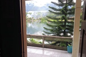 Vista desde una habitación con barandilla de madera que da a una masa de agua, rodeada de vegetación.