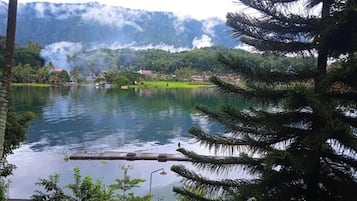 A lake with a dock, surrounded by greenery and mountains in the background.