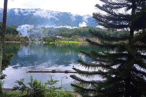 Un lago con un muelle, rodeado de vegetación y montañas al fondo.